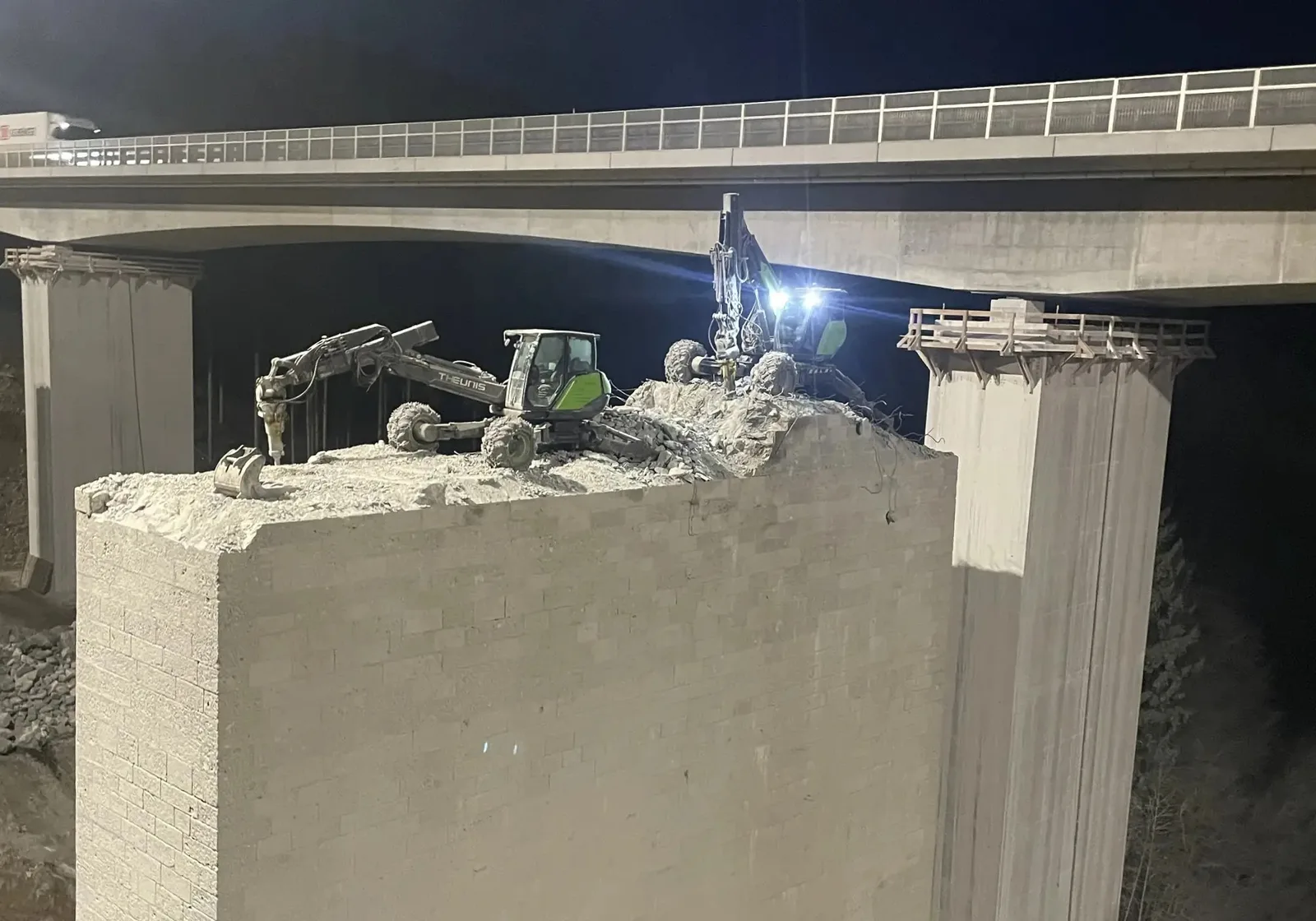 Bagger beim Abbruch eines Brückenpfeilers unter einer Autobahnbrücke bei Nacht