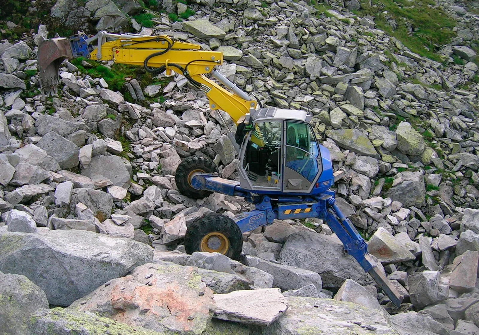 Gelb-blauer Schreitbagger zwischen großen Felsblöcken