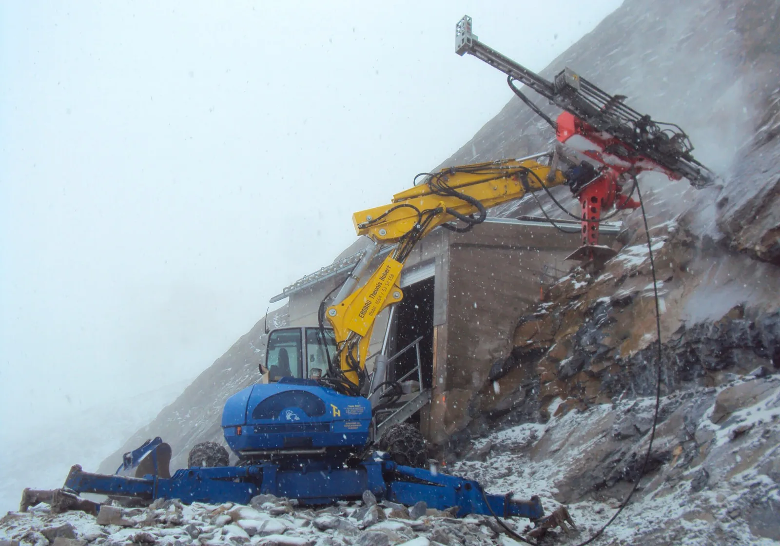 Schreitbagger mit Bohrlafette an einer verschneiten Felswand