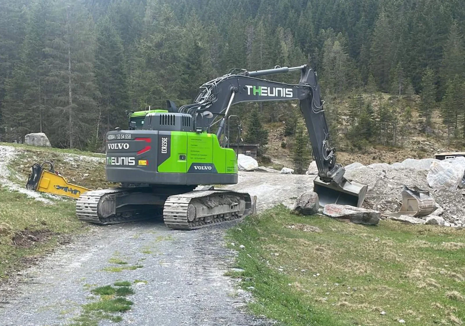 THEUNIS-Kettenbagger auf einem Forstweg neben einem Steinlager