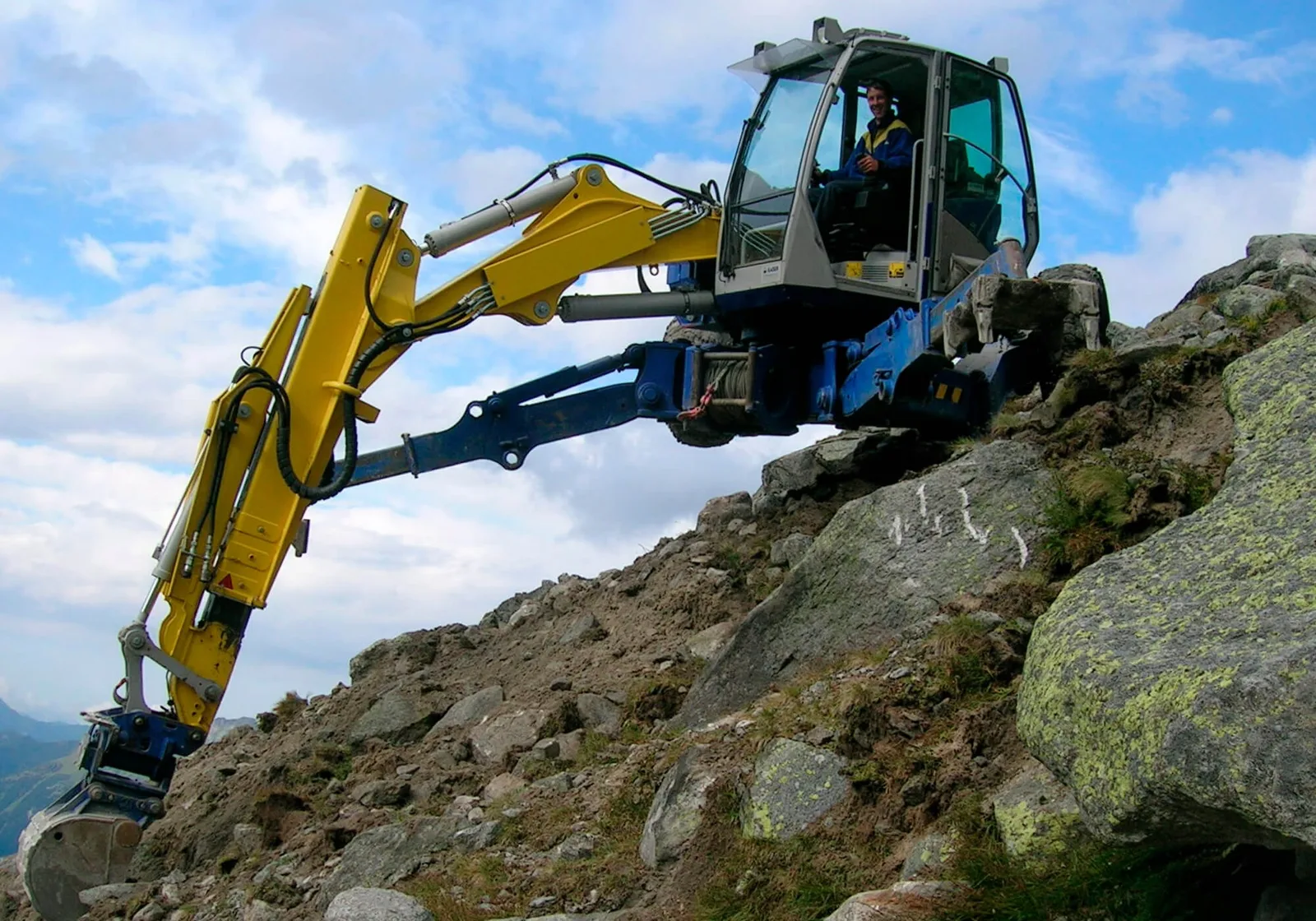 Gelb-blauer Schreitbagger auf einer Felskuppe unter blauem Himmel