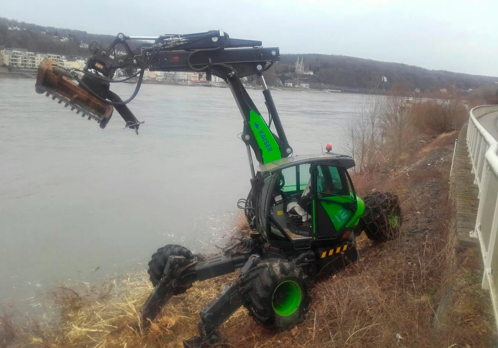 Grüner Schreitbagger mit Mulchkopf am Ufer eines Flusses